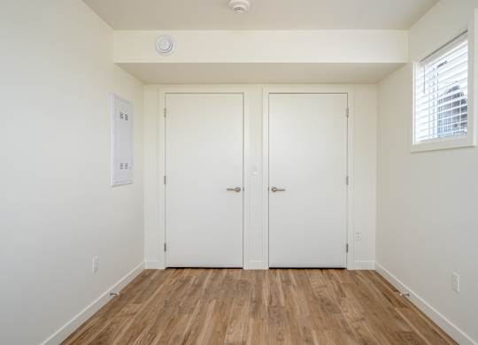 A room with two white doors and a window with blinds.