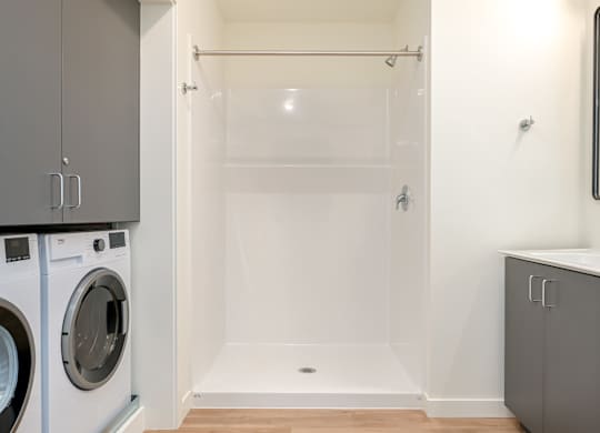 A white bathroom with a walk-in shower and a washer and dryer.