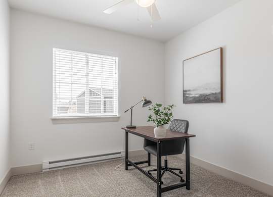 A room with a desk and chair, a plant, and a picture on the wall.