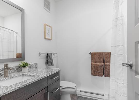 A bathroom with a white toilet, a sink with a mirror above it, and a towel rack with two brown towels.