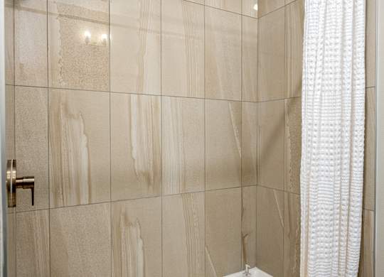 A bathroom with a beige tiled wall and a white shower curtain.