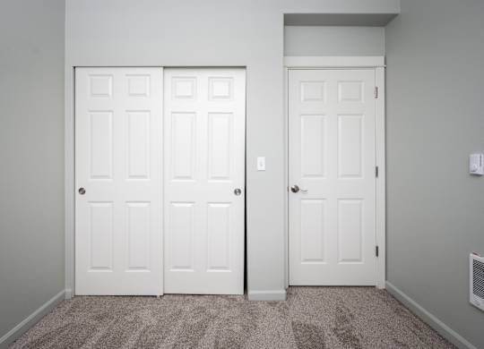 Two white doors in a room with carpeted floor.