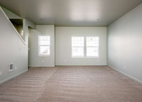 A large empty room with carpeted floor and two windows.