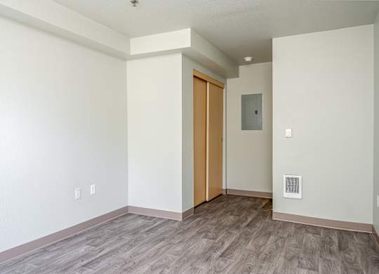 A room with a wooden floor and a white wall with a switchboard and a door.