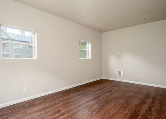 A bedroom with wooden floors and two windows.