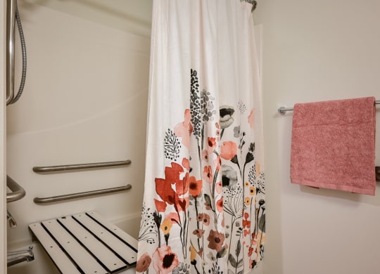 a shower with a floral shower curtain and a pink towel