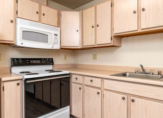 A kitchen with a white microwave oven mounted above a stove and wooden cabinets below.