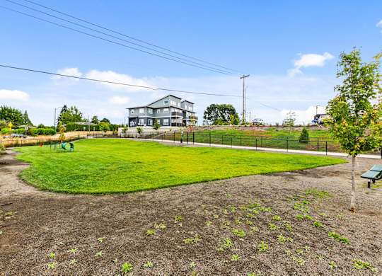 A large grassy field with a fence and a house in the background.