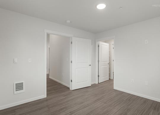 A room with white walls and wooden flooring with two doors.