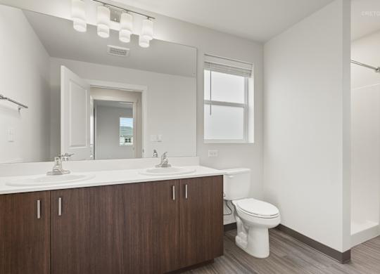A white bathroom with a wooden vanity and a white toilet.