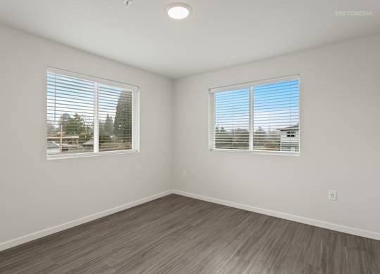 A room with wooden flooring and two windows with blinds.