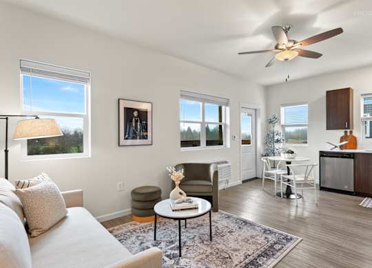A living room with a couch, a table, a fan, and a window.