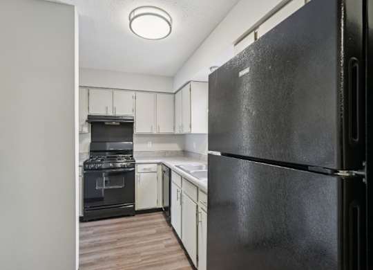 A black refrigerator is in the foreground of a kitchen.