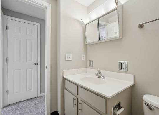 A white bathroom with a sink, mirror, and toilet.