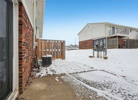 A snow-covered ground with a building and a fence in the background.