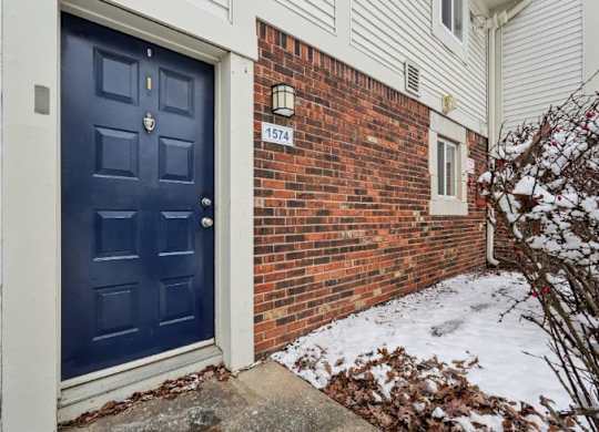 A blue door with a white frame is on the left side of a brick wall with a number 1574 on it.
