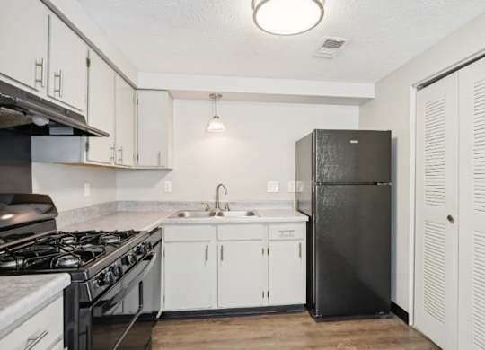 A kitchen with a black refrigerator and white cabinets.