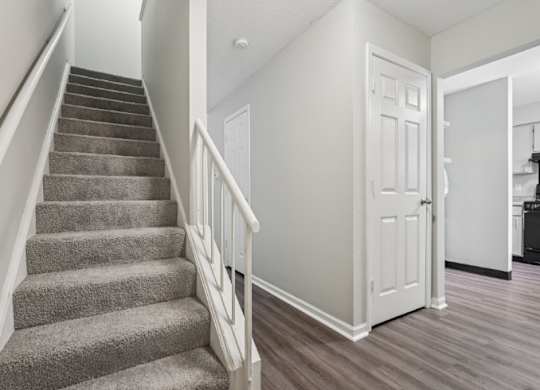 A staircase with a carpeted runner and white balusters leads to a white door.