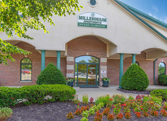 The front of a Millennium Apartments building with a green lawn in front.