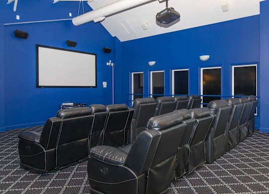 A row of black leather chairs are arranged in front of a white screen in a room with blue walls.