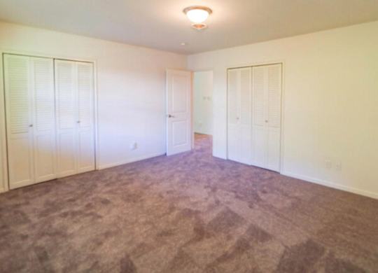 A room with carpeted floor and white walls with three closets.