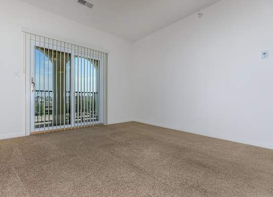 A room with a carpeted floor and a window with a metal grill.