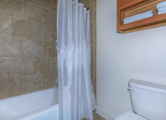 A white shower curtain in a bathroom with a white tub.