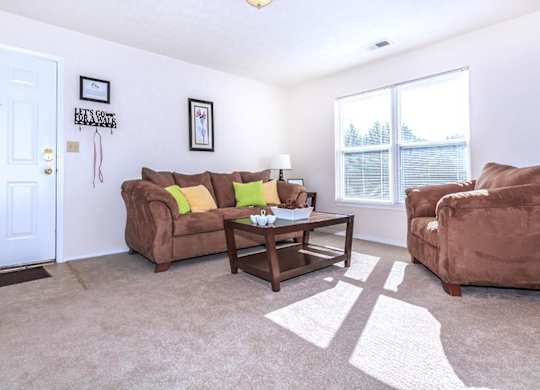 A living room with a brown couch, a coffee table, and a window.