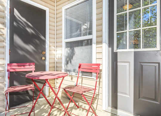 A red table and two chairs are on a porch.