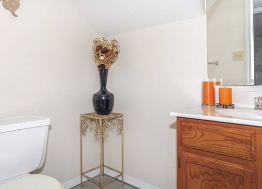 A bathroom with a white bathtub, a wooden vanity, and a vase on a stand.