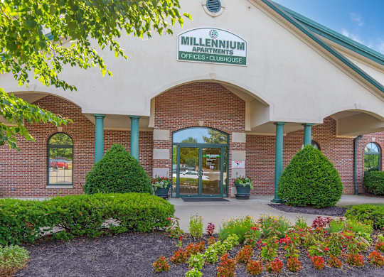 The front of a Millennium Apartments building with a green lawn and flowers in front.