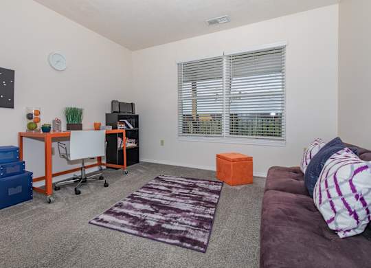 A living room with a purple couch and a white clock on the wall.