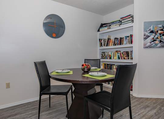 A dining room with a round clock on the wall and a bookshelf with books.