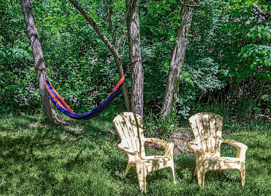 Two plastic chairs are in the foreground of a green forest.