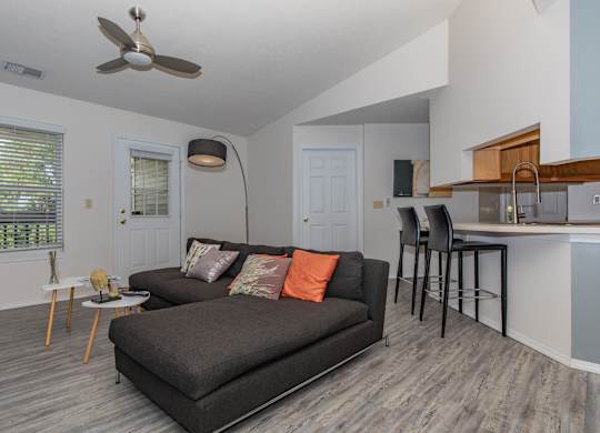 A living room with a grey couch and a fan on the ceiling.
