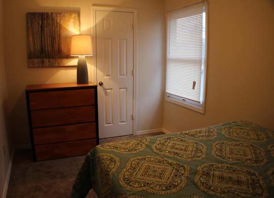 A bedroom with a bed, dresser, and window with blinds.