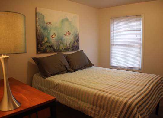A bedroom with a bed, a lamp, and a painting on the wall.