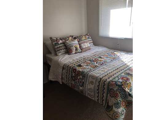 A bed with a white comforter and a multicolored blanket on it.