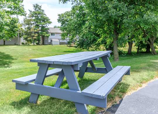 A blue picnic table with a bench in front of a house and trees.