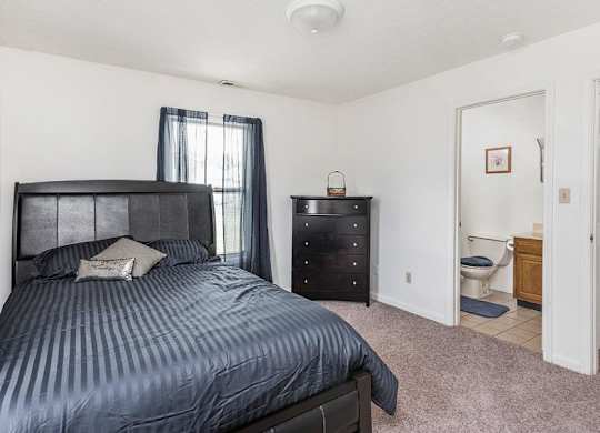 A bedroom with a bed, nightstand, and a small bathroom.