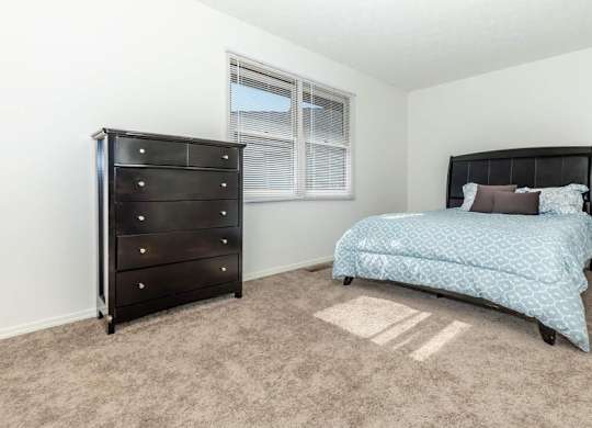 A bedroom with a black dresser and a blue bedspread.