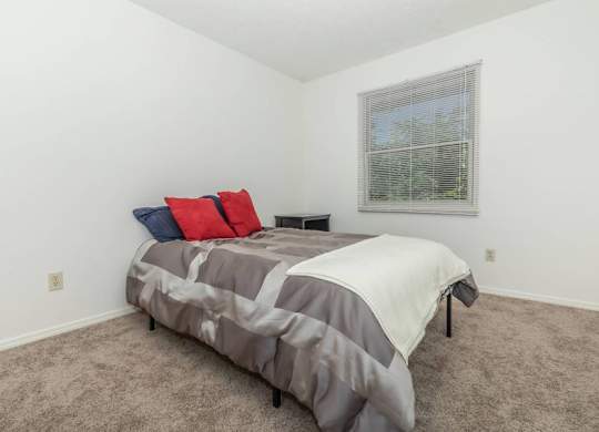 A bedroom with a bed covered in a grey and white comforter and two pillows, one red and one blue.