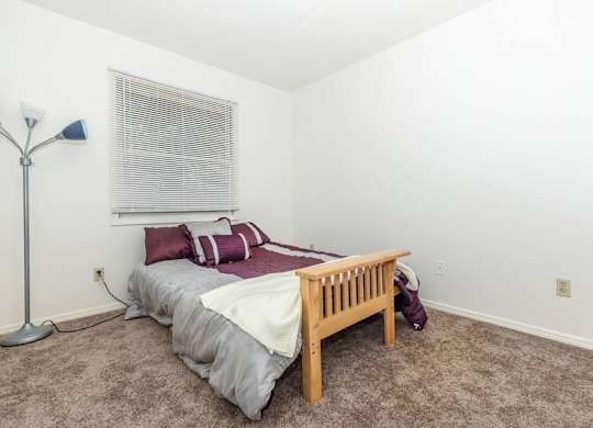 A bedroom with a bed, pillows, a nightstand, and a window with blinds.