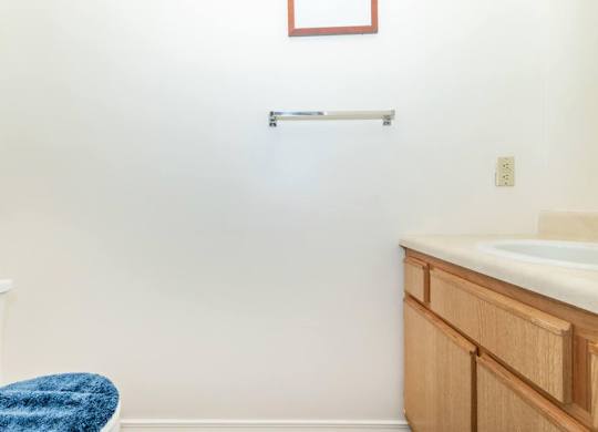 A blue towel is on a white chair in a bathroom with a white sink and wooden cabinet.