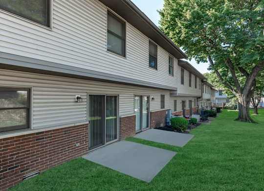 A building with a grey siding and a brick base with a green lawn in front.