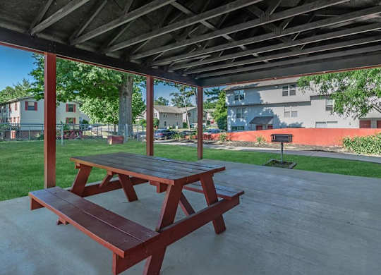 A picnic table under a covered area with a grassy area and buildings in the background.