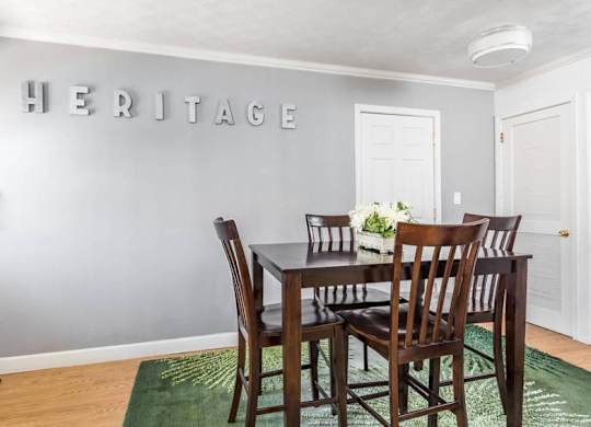 A dining room with a table and chairs and a green rug.