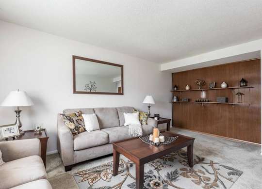 A living room with a grey couch, a wooden coffee table, and a mirror on the wall.