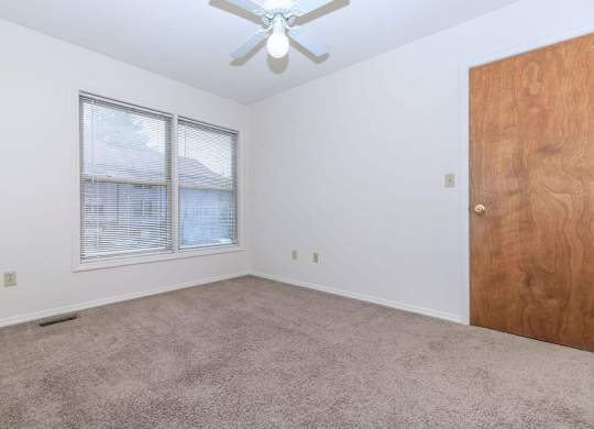 A room with a ceiling fan, carpeted floor, and a wooden door.