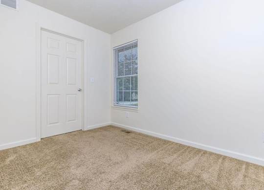 A room with a carpeted floor, a door, and a window with blinds.